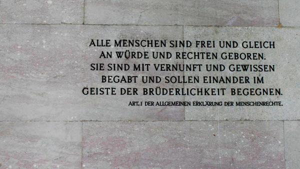 Ein Foto von einer grauen Steinwand, auf der in schwarzen Großbuchstaben der erste Artikel der Menschenrechte steht. 