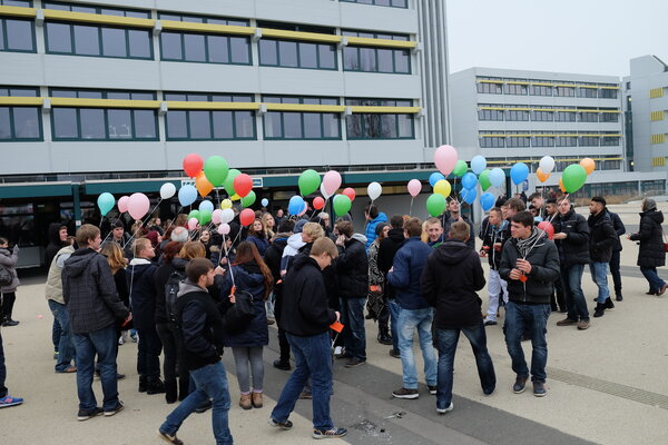 Eine Gruppe von Schüler:innen mit bunte mit Helium gefüllten Luftballons draußen vor einem Schulgebäude